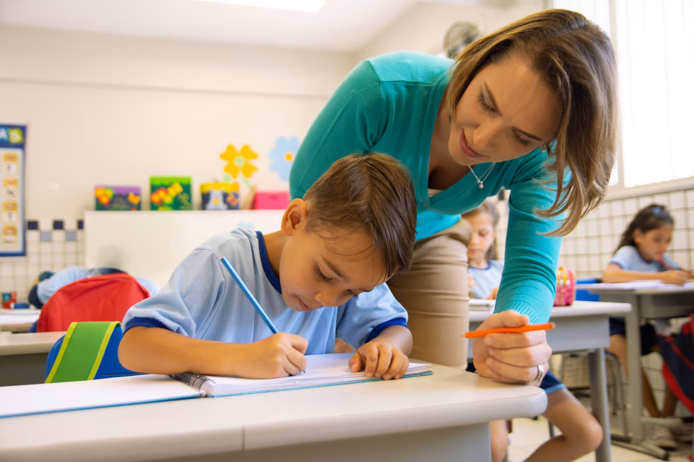 Teacher coaching a student as he writes at his desk